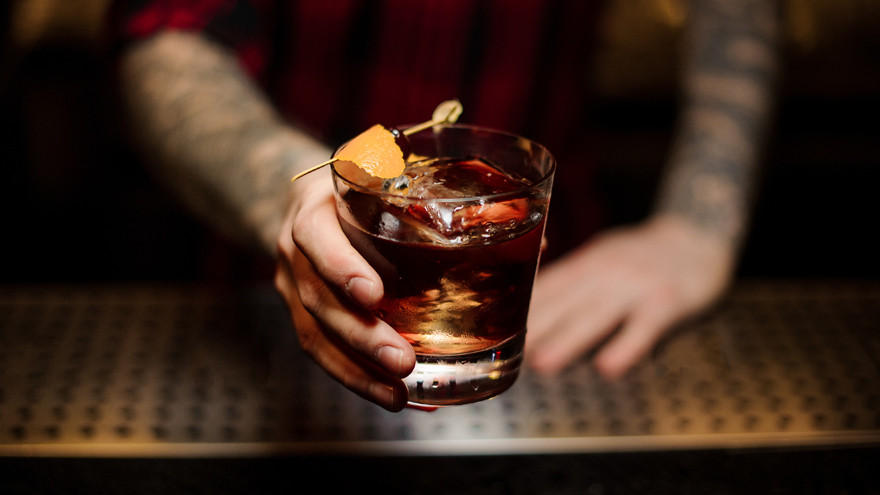 Cocktail met sinaasappelschil wordt aangereikt door barman.