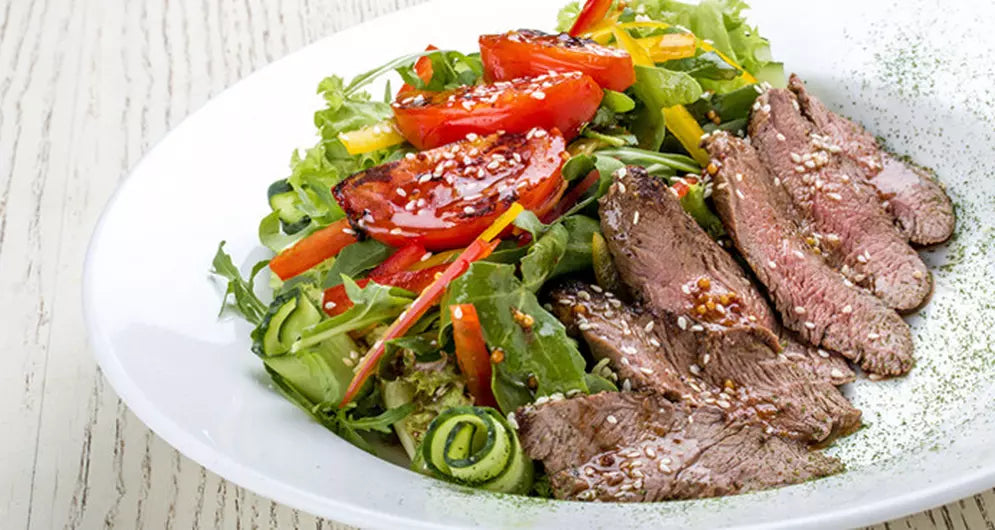 Grilled steak salad with arugula, tomatoes, and sesame seeds.