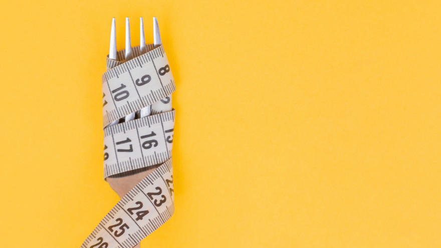 Fork wrapped with measuring tape on yellow background symbolizing diet.