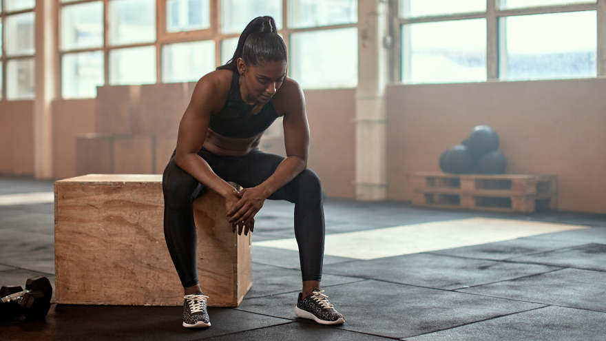Sportlerin im schwarzen Trainingsoutfit sitzt erschöpft auf Box.