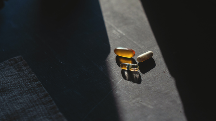 Assorted vitamin and omega capsules on dark surface in natural light.