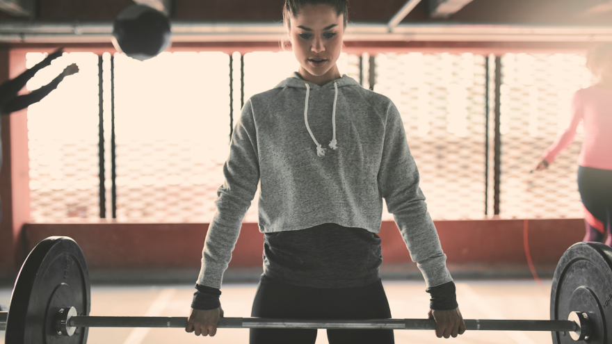 Woman lifting barbell in gym during strength training session.