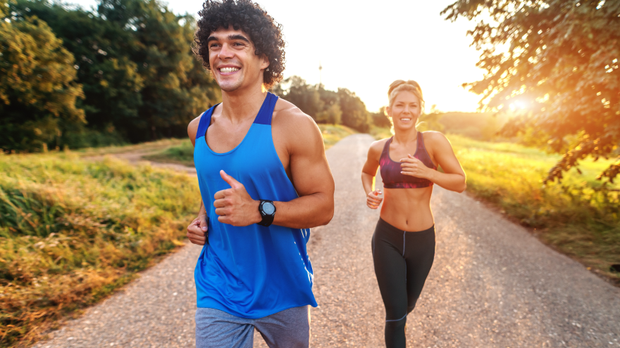 Couple running outdoors on sunny path in fitness attire.