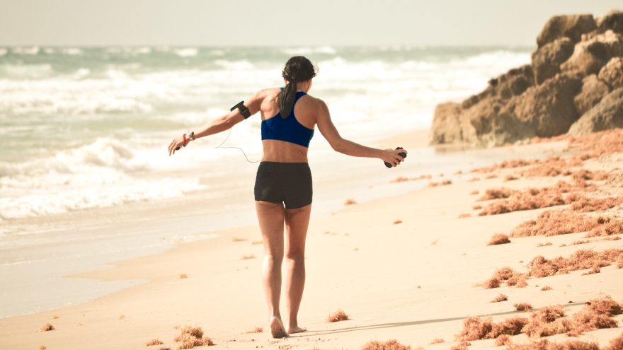 Donna corre sulla spiaggia con auricolari sportivi.