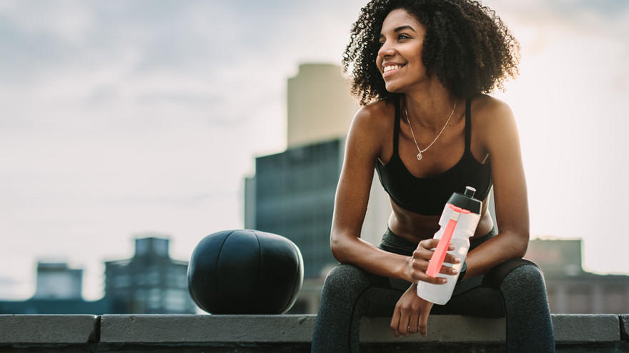 Sportlerin mit Trinkflasche entspannt nach Workout auf Dach.