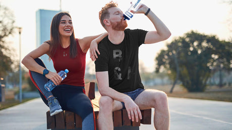 Junges Paar entspannt sich mit Wasserflaschen auf Parkbank nach dem Training.