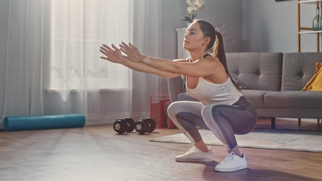 Vrouw doet squats in woonkamer tijdens thuistraining.