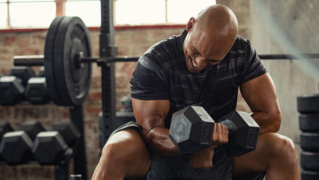 Homme musclé faisant des curls avec haltères en salle de sport.