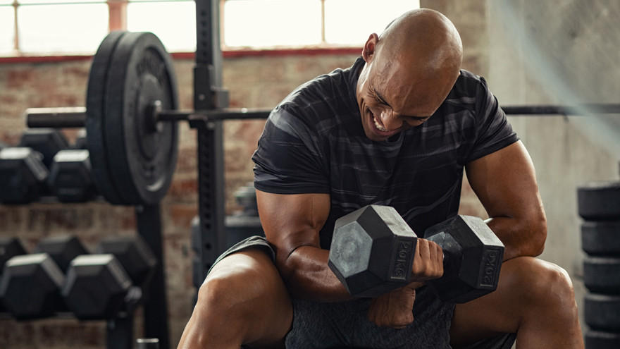Mann trainiert Bizeps mit schwerer Kurzhantel im Gym.
