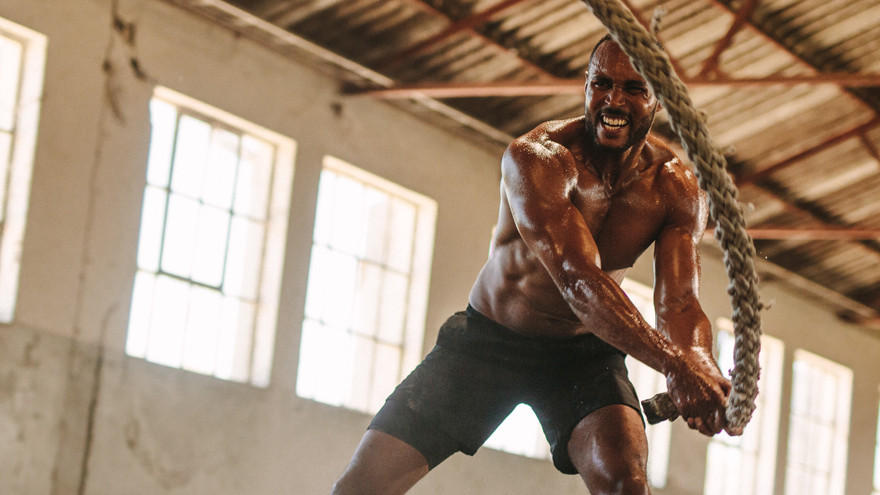 Man training with battle ropes in industrial gym setting.