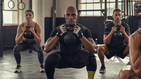 Groupe faisant des squats avec kettlebell en salle de sport.
