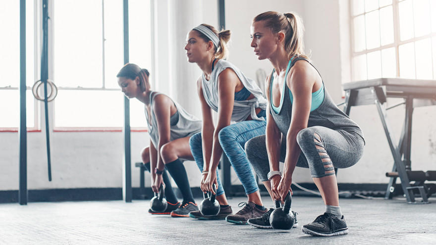 Vrouwen trainen met kettlebells tijdens full-body workout in sportschool.