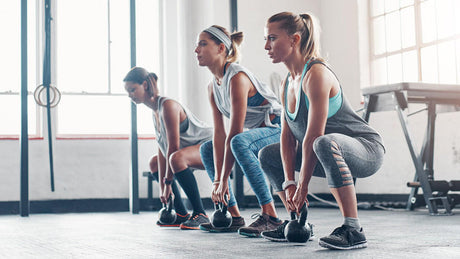 Vrouwen trainen met kettlebells tijdens full-body workout in sportschool.