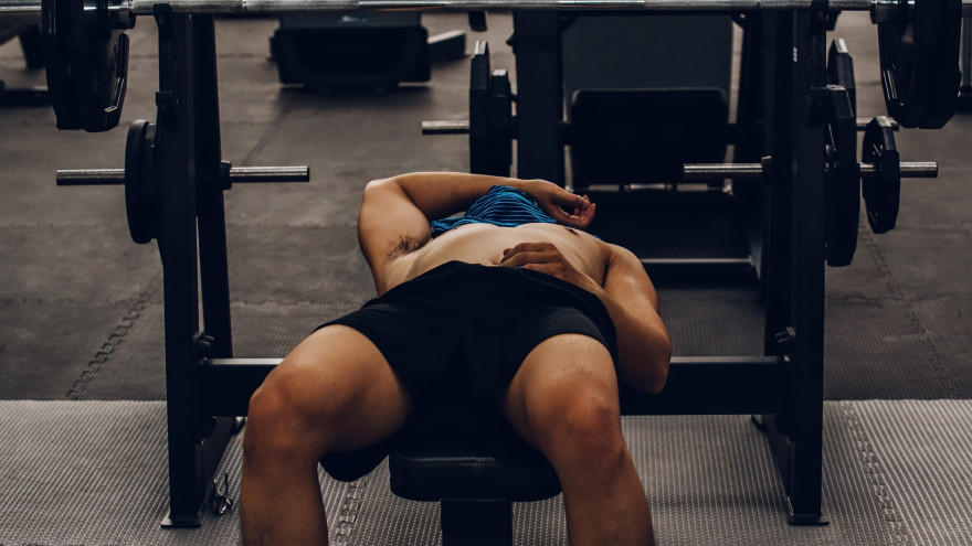 Man ligt uitgeput op bankdrukbank na workout.