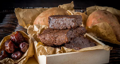 Saftige Schoko-Brownies mit Datteln und Süßkartoffeln auf Backpapier angerichtet.
