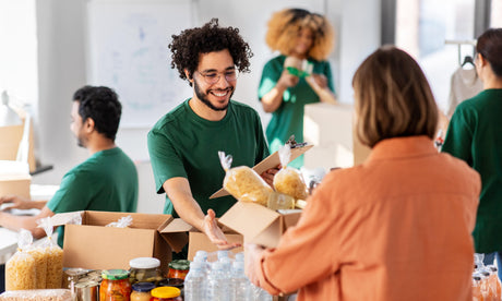 Vrijwilliger overhandigt voedselpakket aan vrouw in distributieruimte.