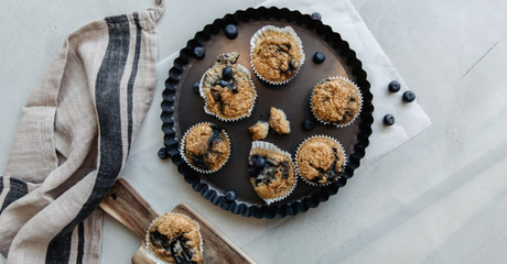 Frische Blaubeer-Muffins auf schwarzem Teller mit Streifenserviette.