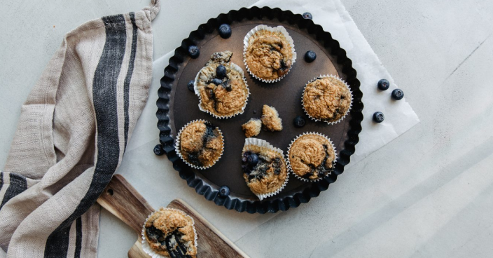 Frische Blaubeer-Muffins auf schwarzem Teller mit Streifenserviette.