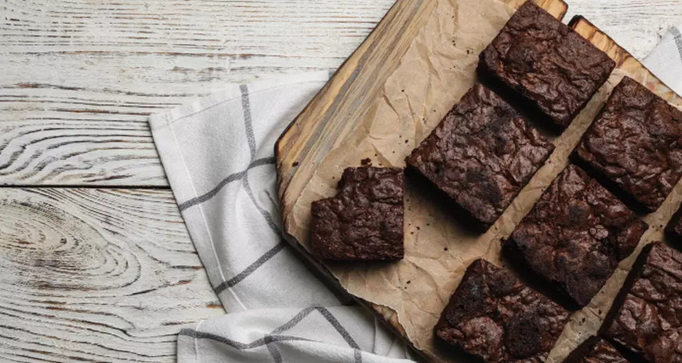 Frisch gebackene, saftige Schokobrownies auf Backpapier und Holzbrett angerichtet.