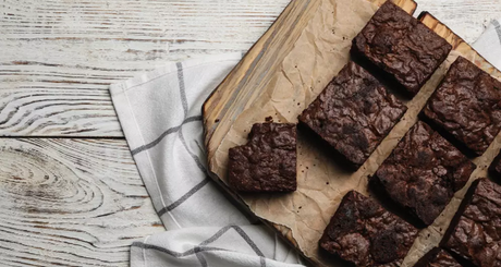 Frisch gebackene, saftige Schokobrownies auf Backpapier und Holzbrett angerichtet.