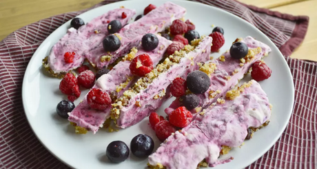 Yoghurtrepen met blauwe bessen en frambozen op wit bord.