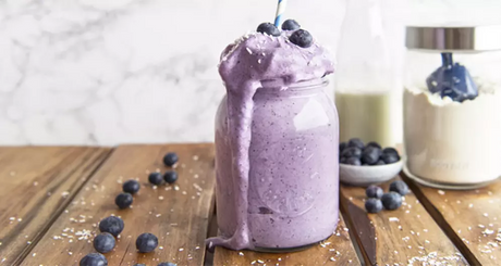 Dikke blauwe bessensmoothie in glazen pot met rietje.