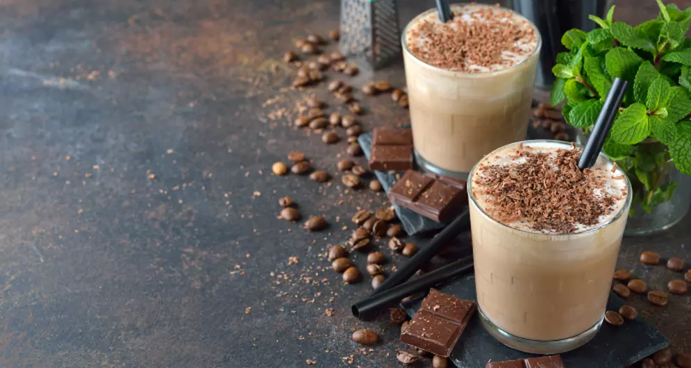 Zwei eisgekühlte Eiskaffee-Drinks mit Schokoladenstückchen auf dunklem Untergrund.