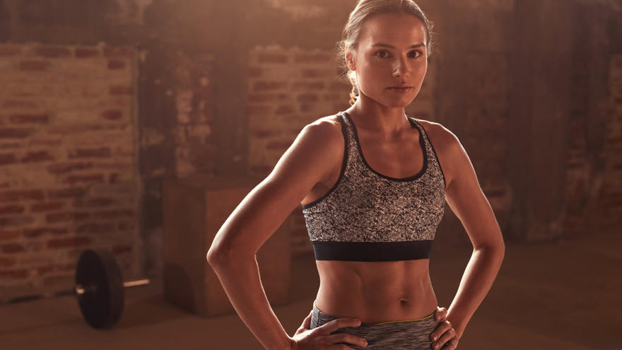 Vrouw in sportbeha poseert in donkere gymzaal.