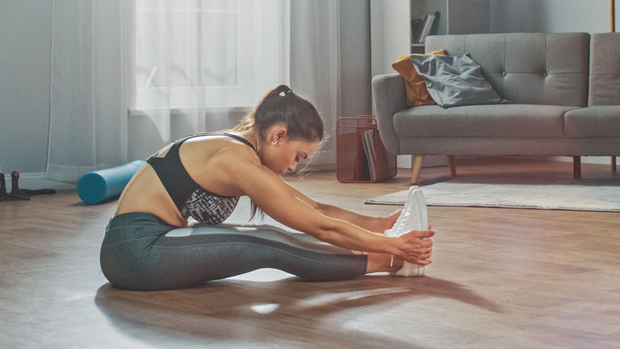 Frau dehnt sich im Wohnzimmer auf Yogamatte.