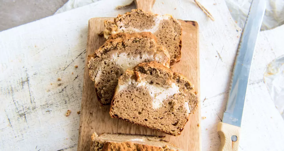 Sliced protein banana bread with cream swirl on wooden cutting board.