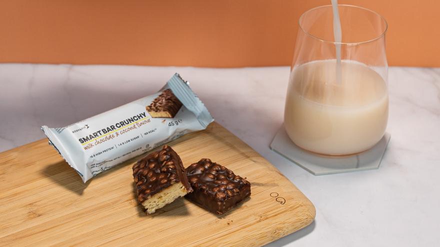 Proteinriegel mit Schokoladenglasur neben Glas Milch.