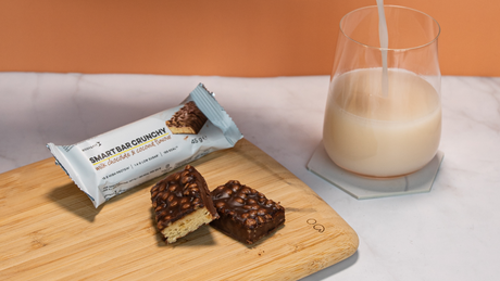Smart Bar Crunchy protein bar with milk on wooden board.