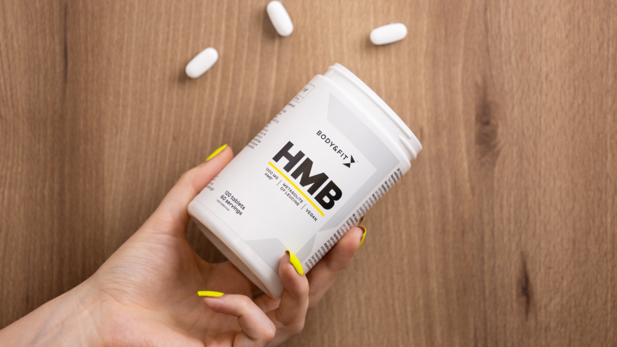 Hand mit Body&Fit HMB-Kapseln auf Holzuntergrund.