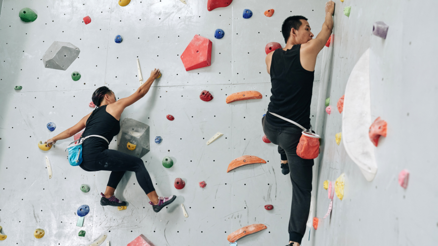 Zwei Personen klettern an Indoor-Boulderwand mit Sicherheitsseil.