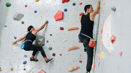 Two people climbing indoor rock wall in black outfits.