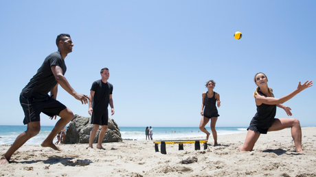 Gruppe junger Erwachsener spielt Spikeball am sonnigen Sandstrand.