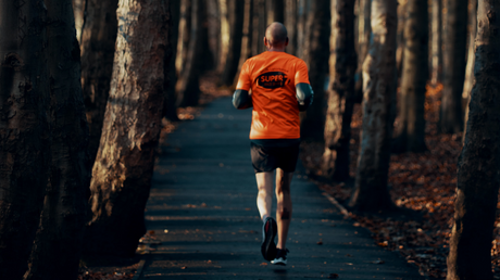 Man jogging on forest trail in orange running shirt.
