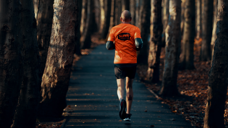 Mann joggt auf Waldweg in orangem Shirt.