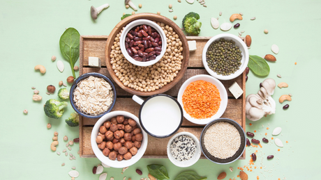 Assortment of plant-based protein sources in bowls on green background.