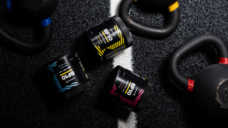 Drei Body&Fit Booster-Dosen neben Kettlebells auf Boden.