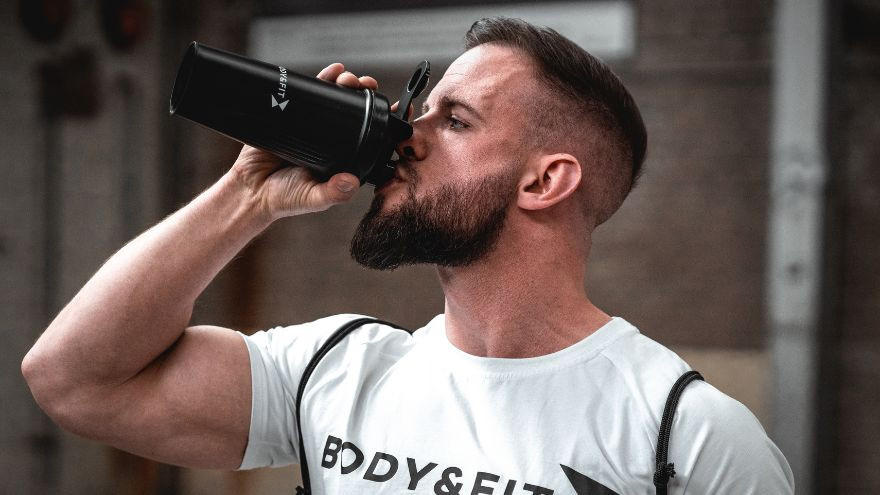 Sportler trinkt Shake im Fitnessstudio mit Body&Fit Shirt.