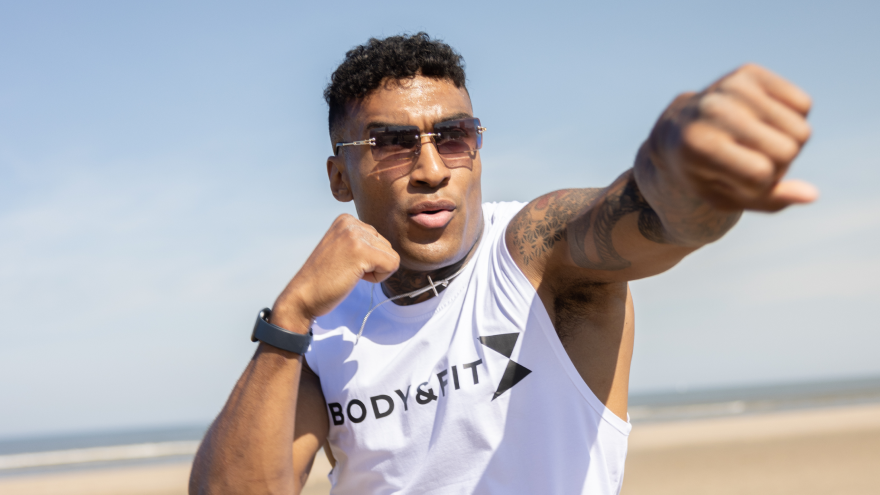 Mann boxt am Strand in ärmellosem Body&Fit-Shirt.