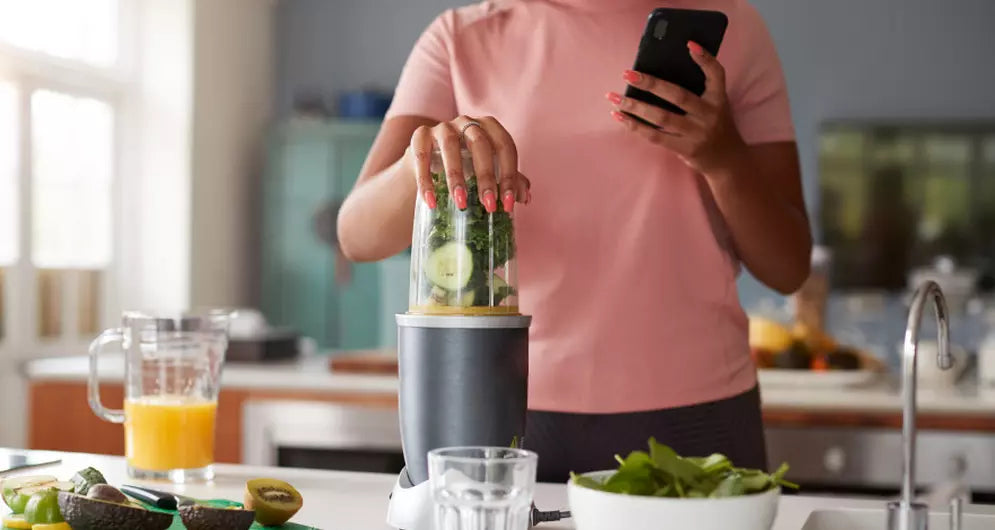 Femme préparant un smoothie vert avec un blender.