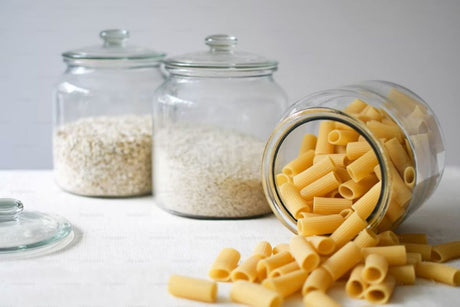 Bocaux en verre remplis de flocons d'avoine et de riz et un bocal renversé de rigatoni, des aliments riches en glucides pour la recharge glucidique