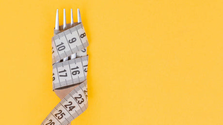 Fork wrapped with measuring tape on yellow background symbolizing diet.