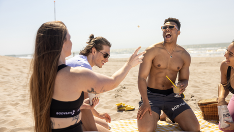 Friends having fun at beach picnic with Body&Fit snacks.