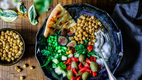 Vegetarische Bowl mit Kichererbsen, Gemüse und Fladenbrot auf Holztisch.