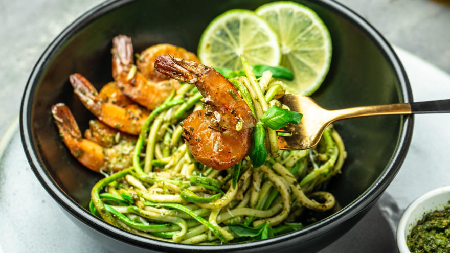 Courgettepasta met garnalen, pesto en limoenschijfjes in zwarte kom.