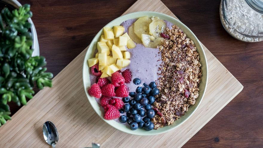 Smoothiebowl mit Müsli, Himbeeren, Mango, Banane und Blaubeeren.