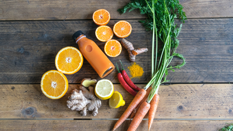 Karotten, Orangen und Ingwer mit Flasche Saft auf Holz.